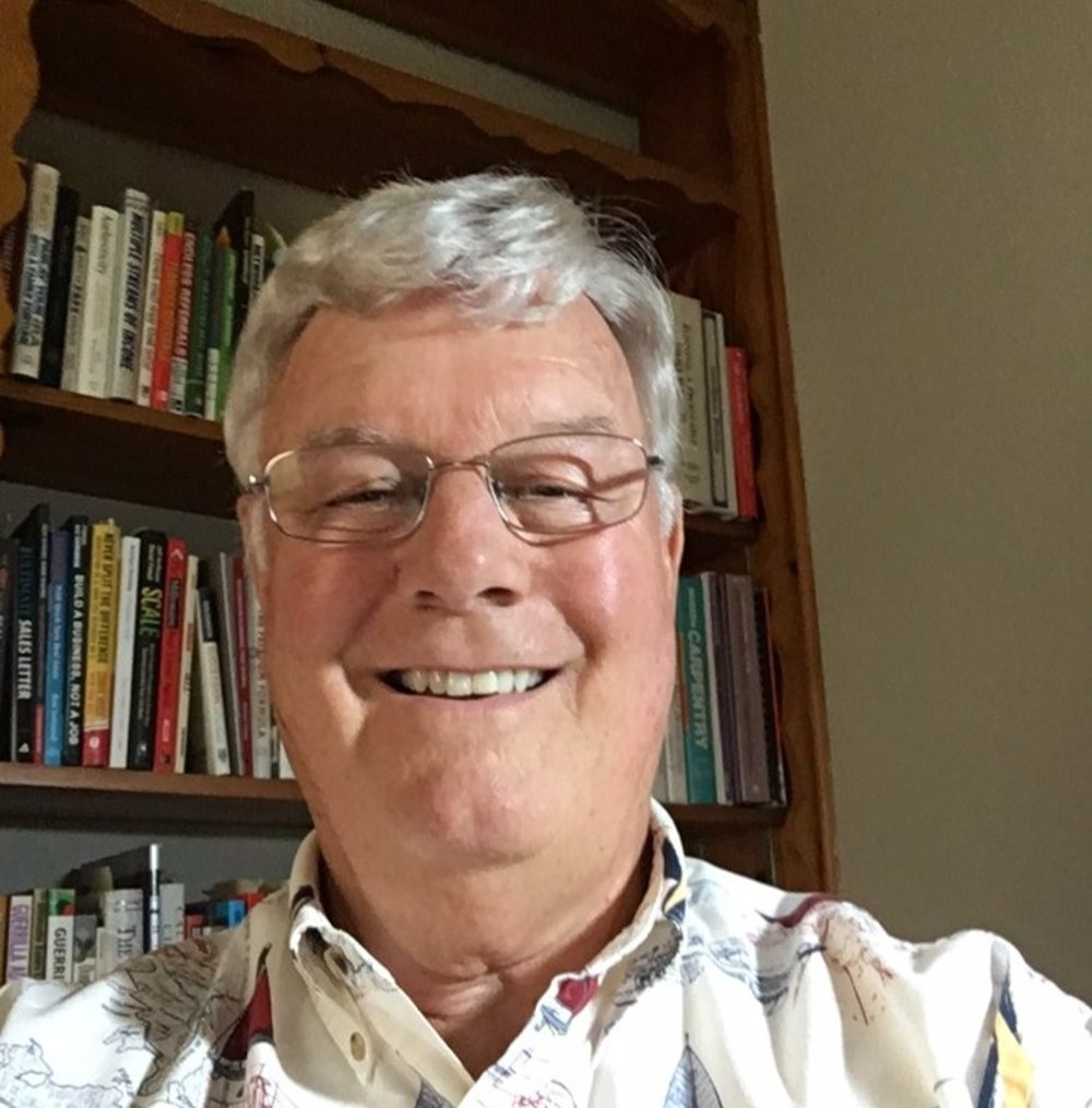 A man with glasses and a shirt on in front of a bookshelf.